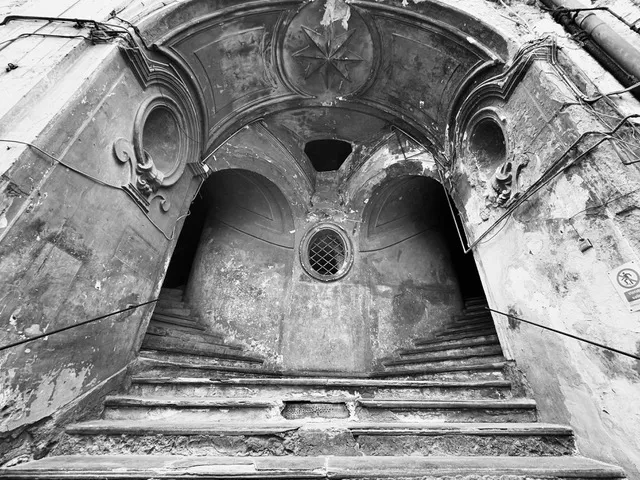 Scala in pietra ripresa dal basso sotto volte ad arco, con stella in rilievo e finestrella tonda al centro, in bianco e nero