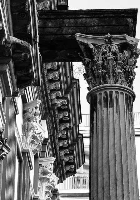 Capitelli corinzi e trabeazione di un pronao ripresi dal basso, con le mensole del cornicione in prospettiva, in bianco e nero