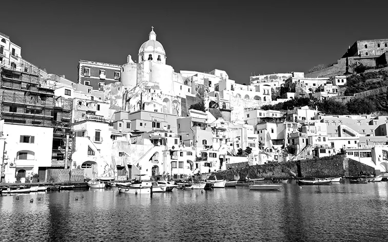 Case addossate sulla collina sopra una marina con barche ormeggiate e una cupola, in bianco e nero