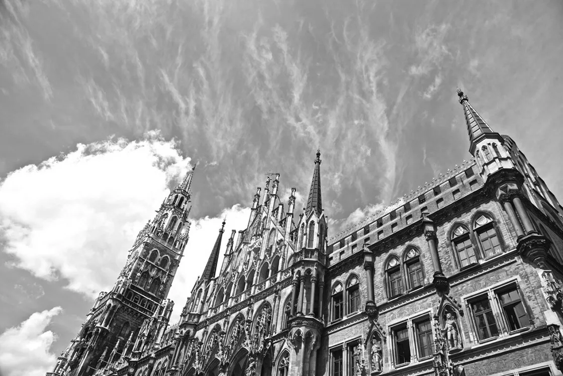 Facciata neogotica con guglie e alta torre vista dal basso contro un cielo con nuvole leggere, in bianco e nero