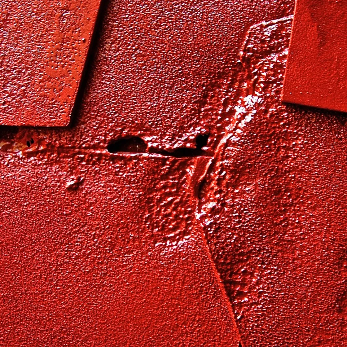 Superficie rossa lucida e granulosa attraversata da una cresta diagonale e piccoli fori