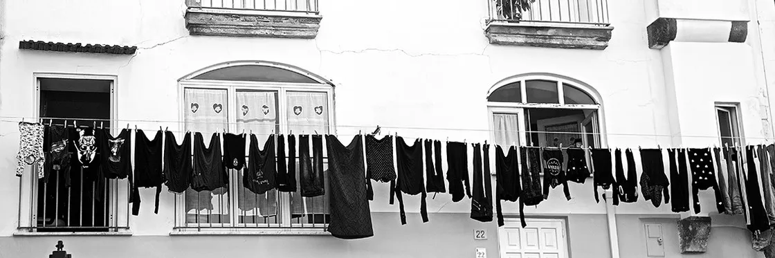 Panni scuri stesi ad asciugare su un filo davanti alla facciata bianca di un edificio, in bianco e nero