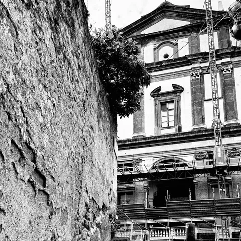 Antica muratura in primo piano e, dietro, la facciata di una chiesa avvolta dai ponteggi di un restauro, in bianco e nero