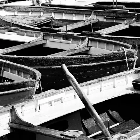 Dettaglio di barche a remi in legno accostate, scafi sovrapposti e un remo appoggiato di traverso, in bianco e nero