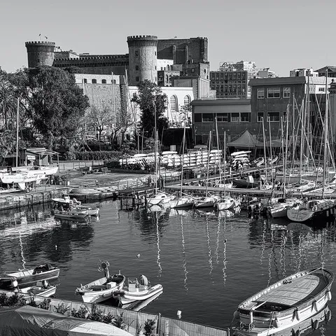 Le torri di Castel Nuovo alle spalle del porticciolo, con barche e alberi di velieri riflessi nell'acqua, in bianco e nero