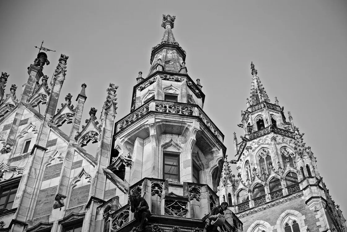 Guglie e pinnacoli neogotici con statue e torre ripresi dal basso contro il cielo, in bianco e nero
