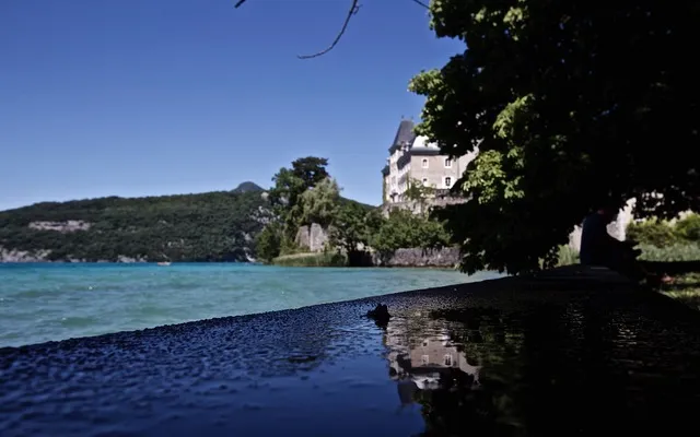 Lago dalle acque turchesi con un castello su un promontorio alberato e una persona seduta all'ombra sulla riva