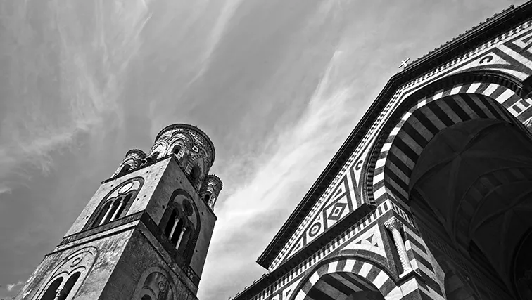 Campanile e facciata a fasce di una cattedrale visti dal basso contro il cielo, in bianco e nero