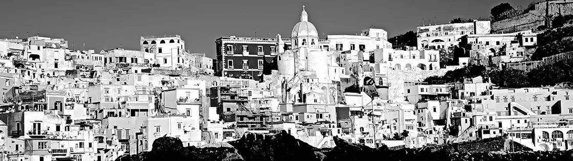 Veduta panoramica delle case fitte di un paese collinare con una cupola al centro, in bianco e nero