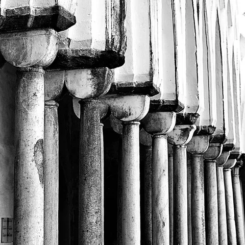 Fila di colonne in pietra con capitelli che si allontana in prospettiva lungo un colonnato, in bianco e nero