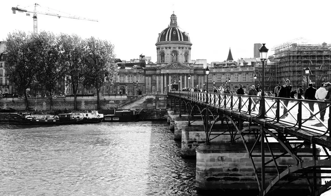Ponte pedonale sulla Senna con passanti, palazzo con cupola e chiatte ormeggiate sullo sfondo, in bianco e nero