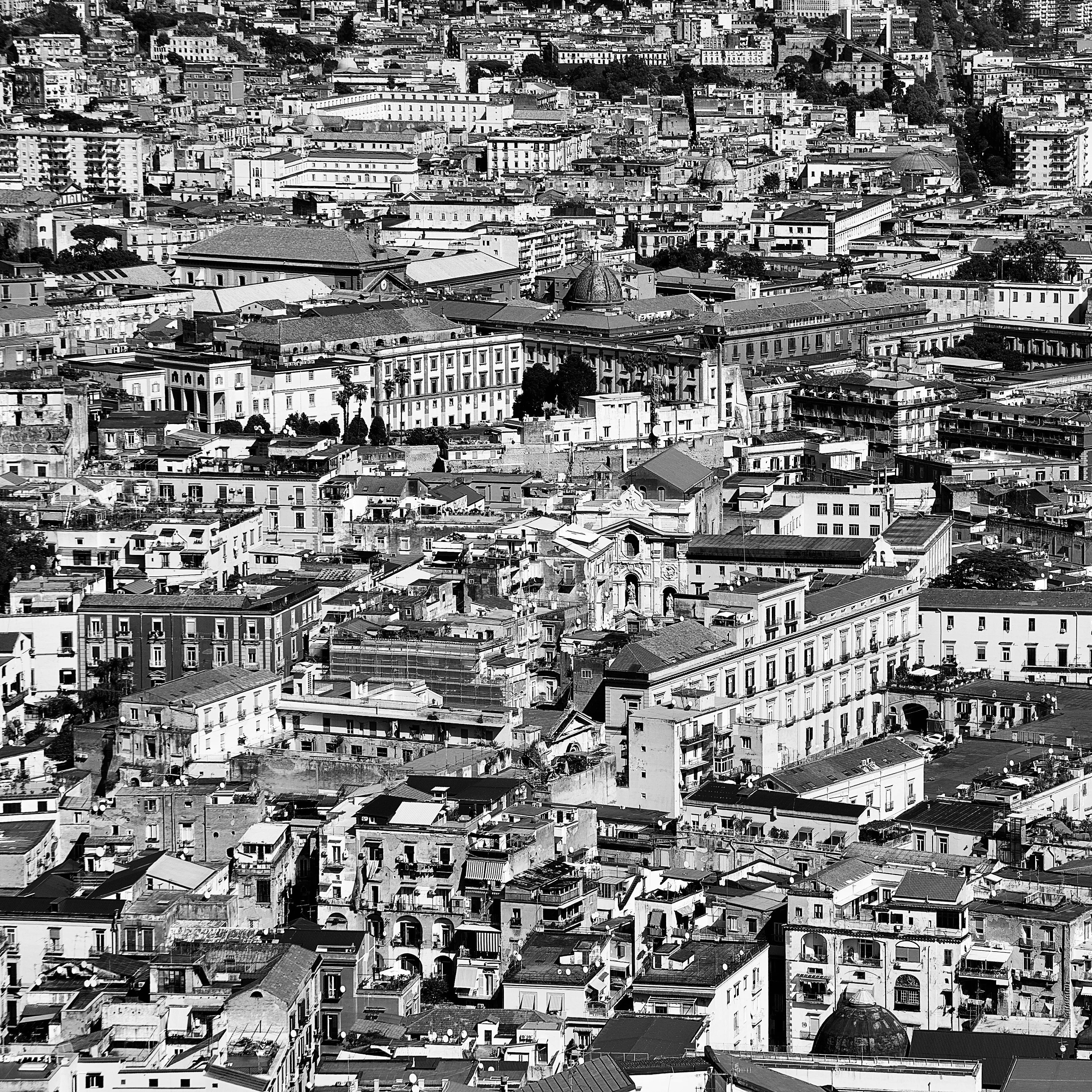 Veduta dall'alto di una città densa di edifici e tetti che si estende fino all'orizzonte, in bianco e nero