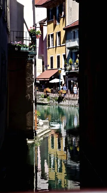 Scorcio di un canale tra edifici colorati con fiori, ombrelloni e persone riflessi nell'acqua