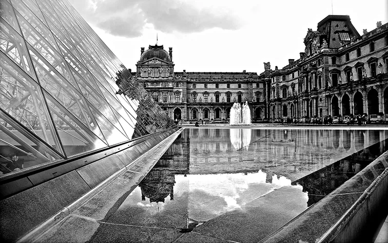 Piramide di vetro e facciata di un museo riflesse in una vasca con fontana, in bianco e nero
