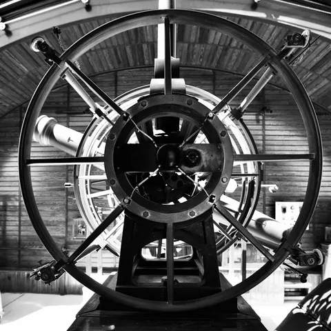 Grande telescopio storico dentro un osservatorio dalle pareti in legno, visto frontalmente, in bianco e nero