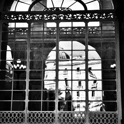 Grande vetrata ad arco in ferro attraverso cui si intravede un edificio con cupola all'esterno, in bianco e nero