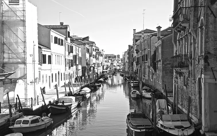 Canale fiancheggiato da vecchi edifici e barche ormeggiate, in bianco e nero