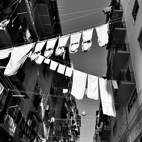 Panni stesi su fili tesi tra i palazzi di un vicolo stretto, ripresi dal basso verso il cielo, in bianco e nero