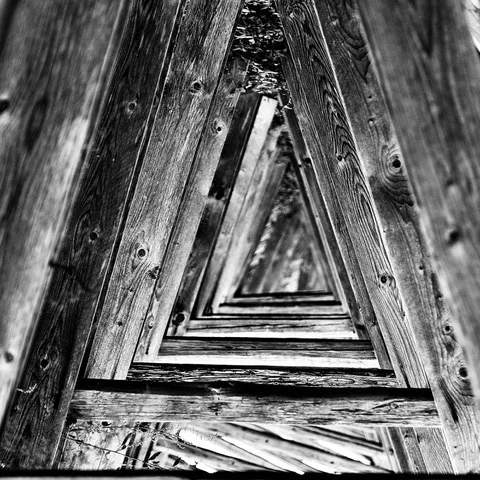 Vista prospettica dentro una struttura in legno, le assi convergono formando triangoli concentrici, in bianco e nero