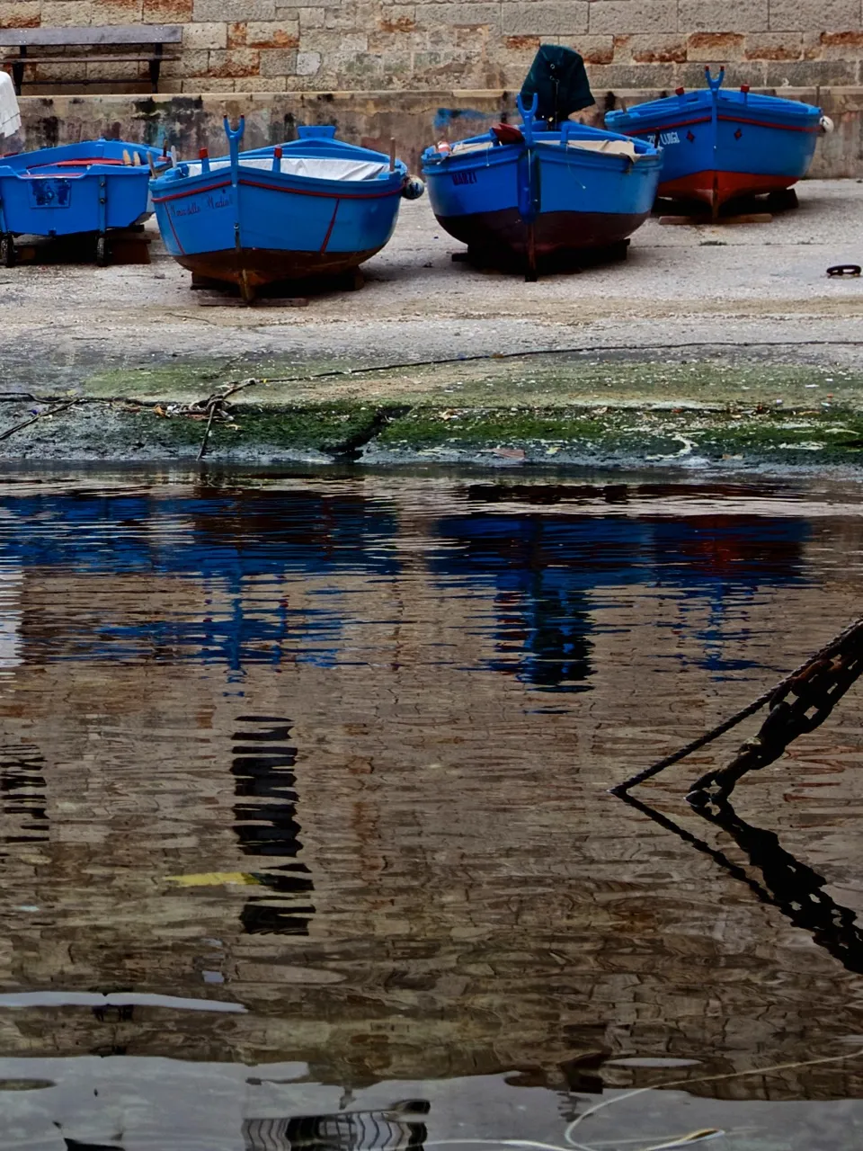 Barche da pesca azzurre tirate in secca su una banchina, con i loro riflessi che ondeggiano nell'acqua