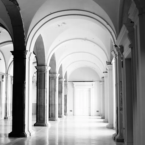 Luminoso corridoio voltato con archi e colonne e una porta in fondo, dai toni chiari e delicati, in bianco e nero