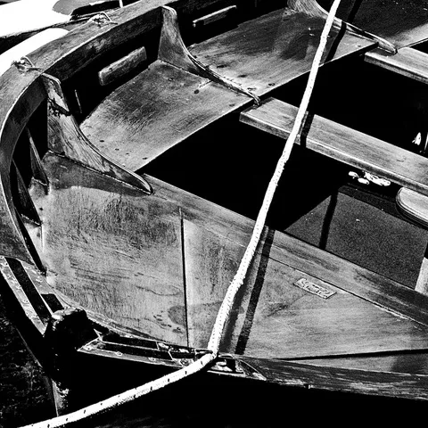 Dettaglio dell'interno di una barca di legno, con una cima bianca che l'attraversa in diagonale, in bianco e nero