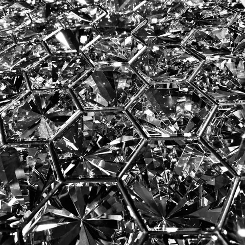 Primo piano di prismi di cristallo sfaccettati disposti in forme esagonali che riflettono la luce, in bianco e nero