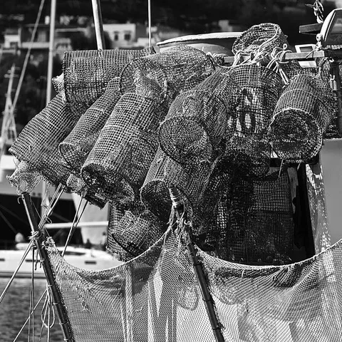 Nasse a rete metallica accatastate su una barca con le reti da pesca, il porto sfocato sullo sfondo, in bianco e nero