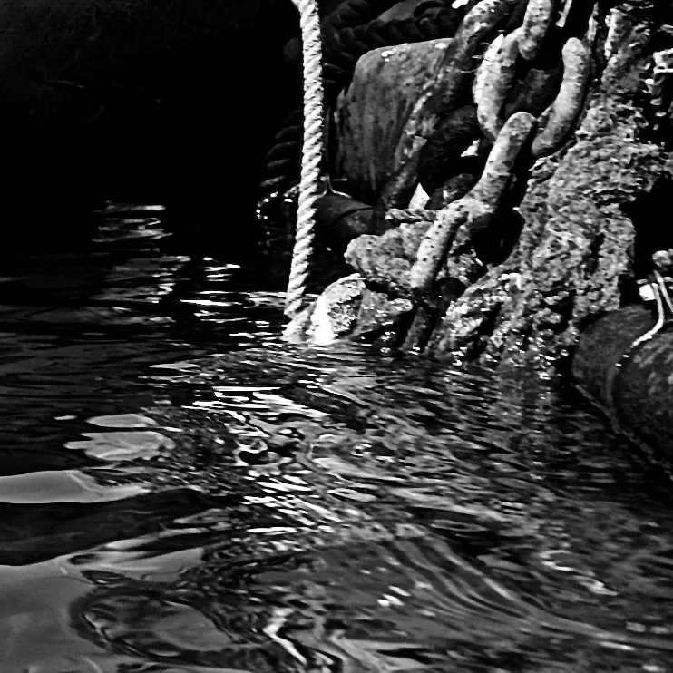 Catene arrugginite e una fune calano nell'acqua scura di un ormeggio, in primo piano ravvicinato, in bianco e nero
