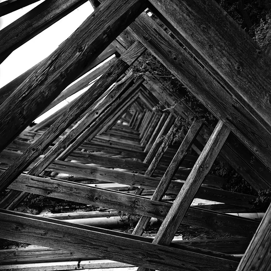 Struttura di travi di legno che si ripetono in prospettiva formando un tunnel di riquadri, in bianco e nero