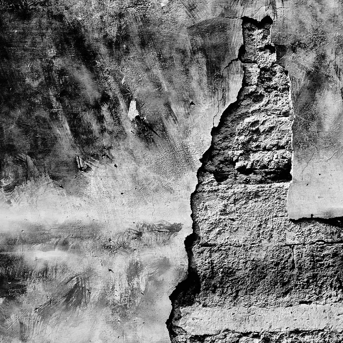 Muro intonacato e sgretolato con una grande crepa che scopre i mattoni sottostanti, in bianco e nero
